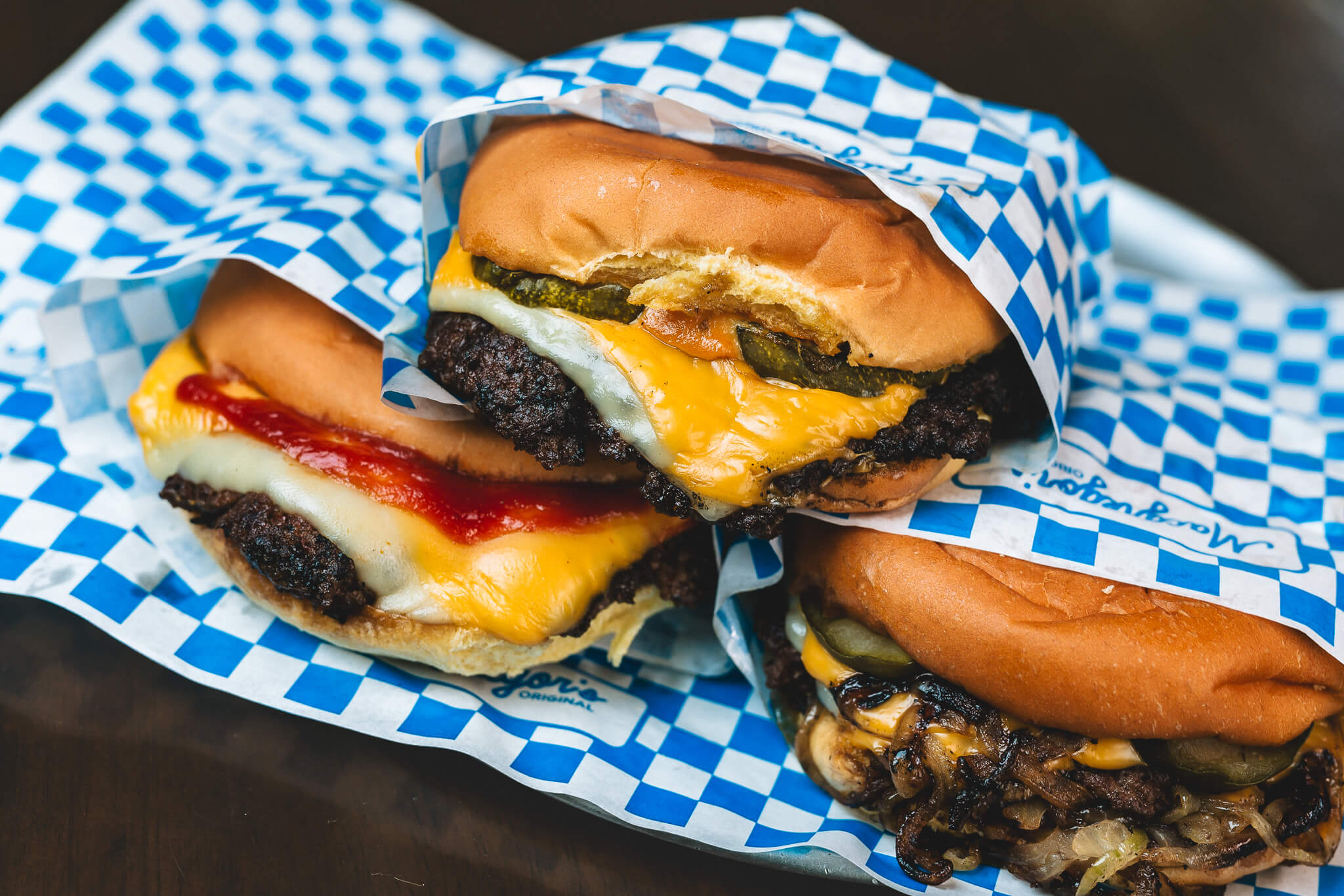 Three Macgregor's smash burgers in blue-checkered wrappers — cheese, pickles and caramelised onions.