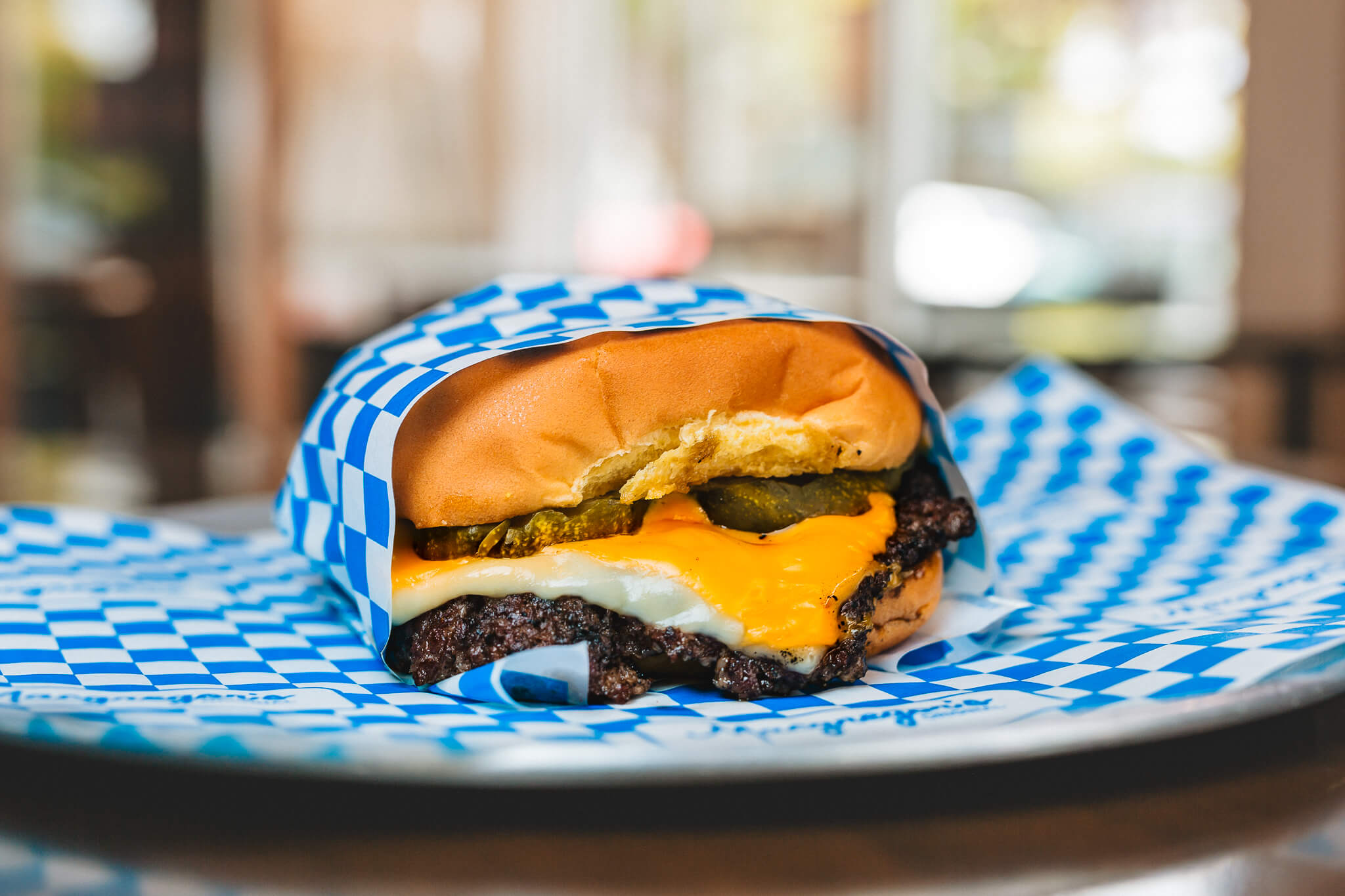 A Macgregor's smash burger — melty cheese, pickles and a crispy onion on a toasted Martin's roll, wrapped in blue-checkered paper.